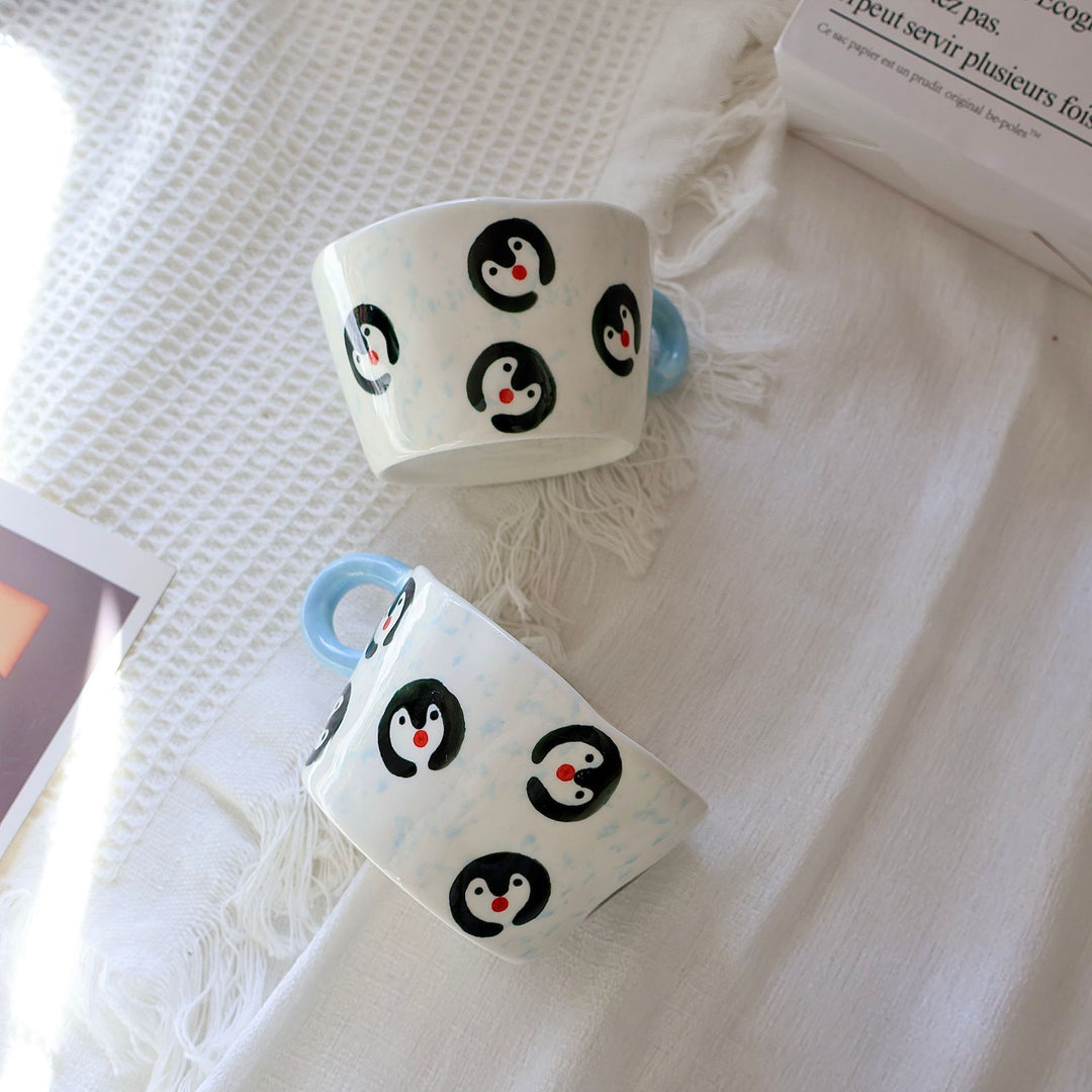 Ceramic coffee mug with hand-painted penguin designs and ergonomic handle