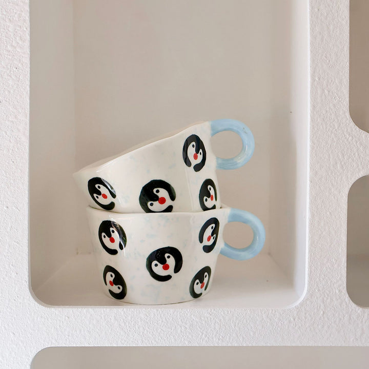Ceramic coffee mug with hand-painted penguin designs and ergonomic handle