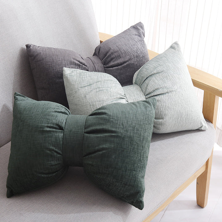 Bow-shaped decorative cushion with central band detail and structured fabric look