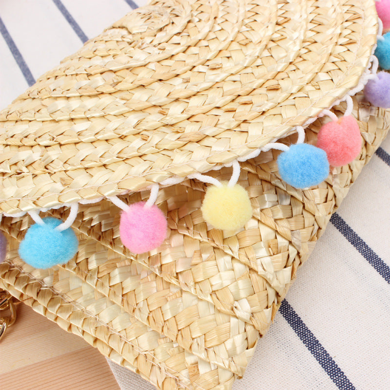 Clutch made of handwoven natural material with decorative pompons Kalsten