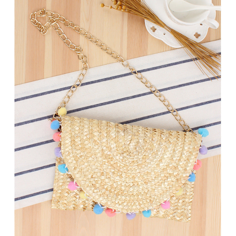 Clutch made of handwoven natural material with decorative pompons Kalsten